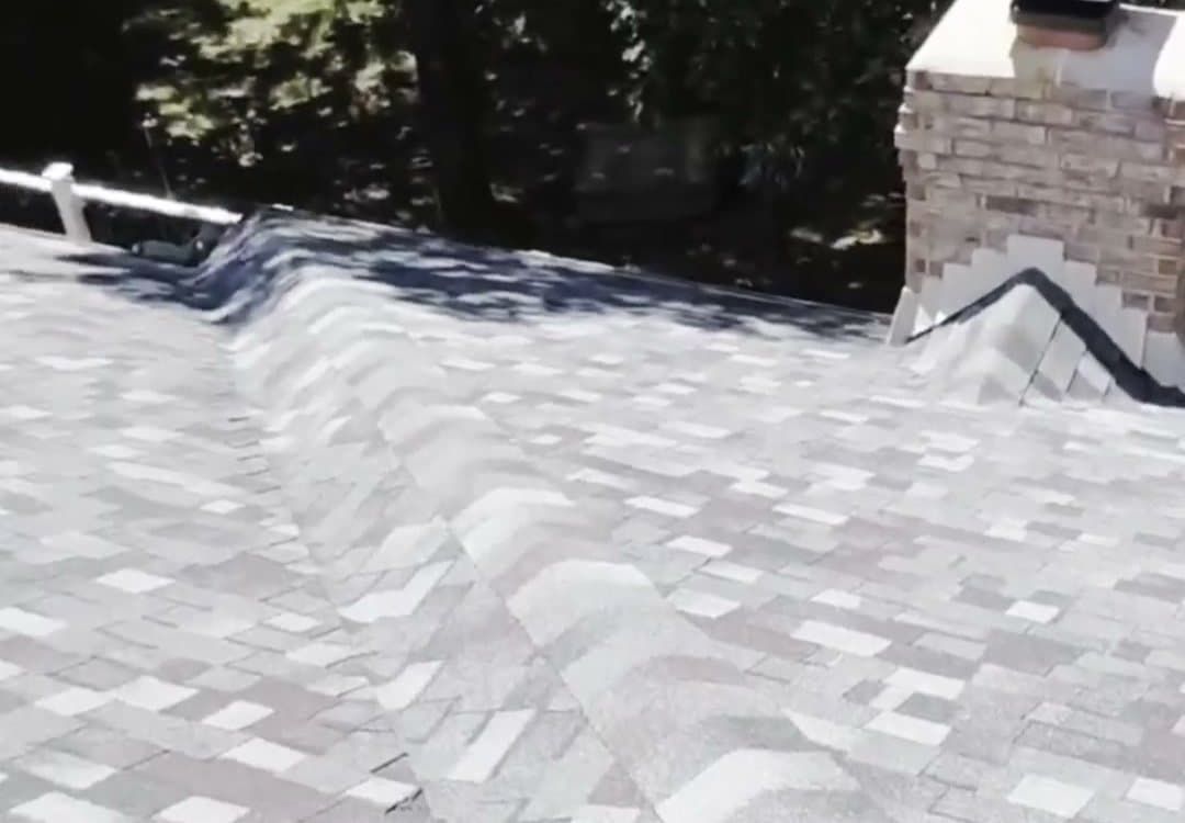 A finished architectural shingle roof by Sobczak Exteriors, ridge and brick chimney flashing, on a wooded lot