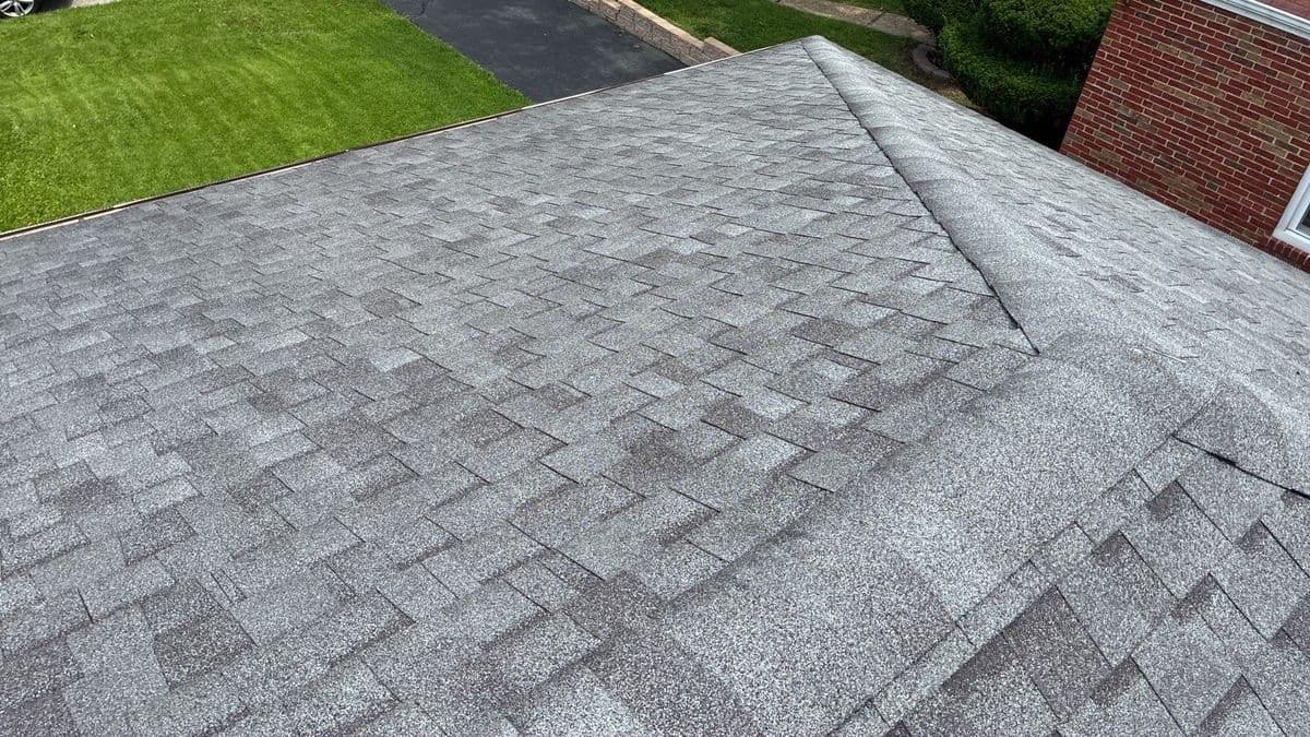Finished grey architectural shingle roof seen from the ridge, capped hip running down to the eave
