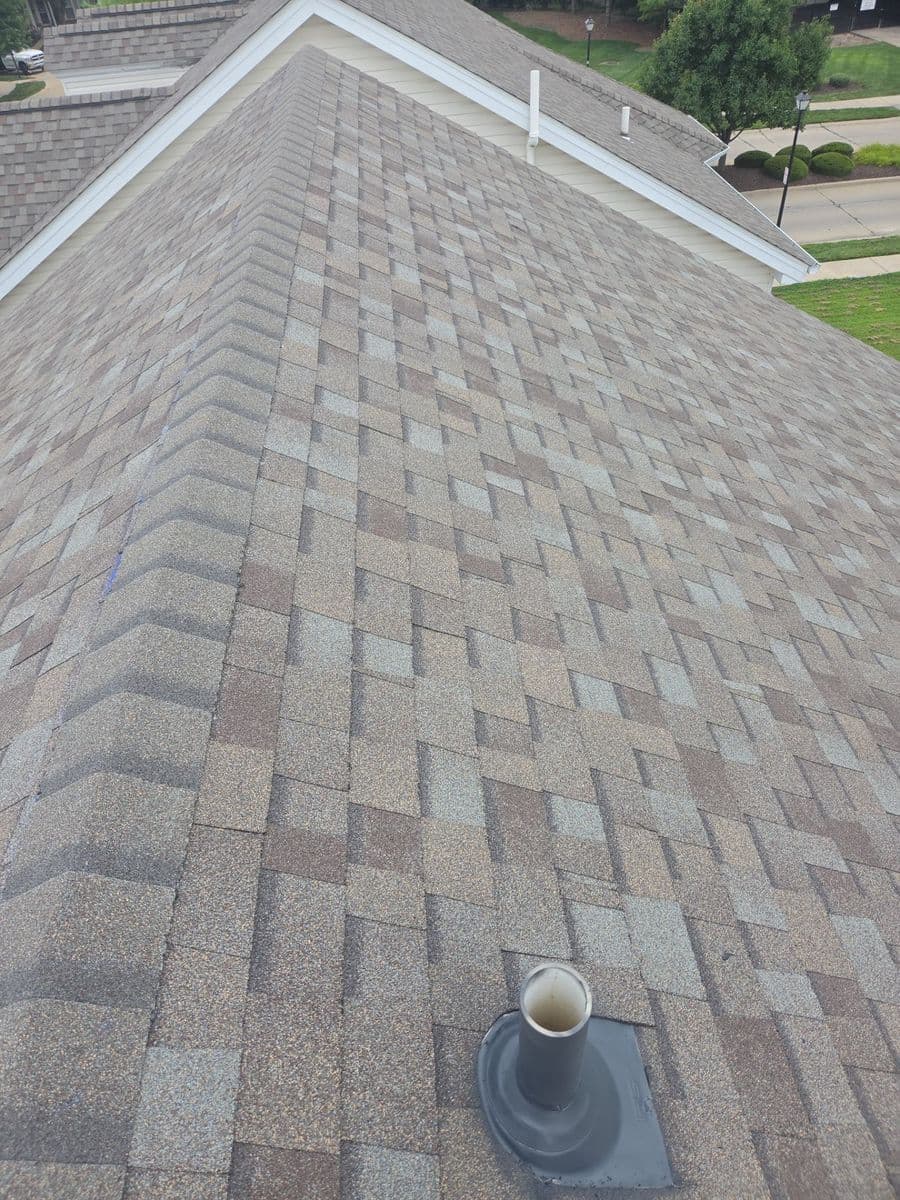 Long run of finished weathered-wood blend shingles up to the ridge, pipe boot flashed in