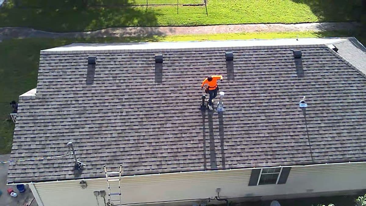 Overhead view of a crew member working across a grey shingle roof