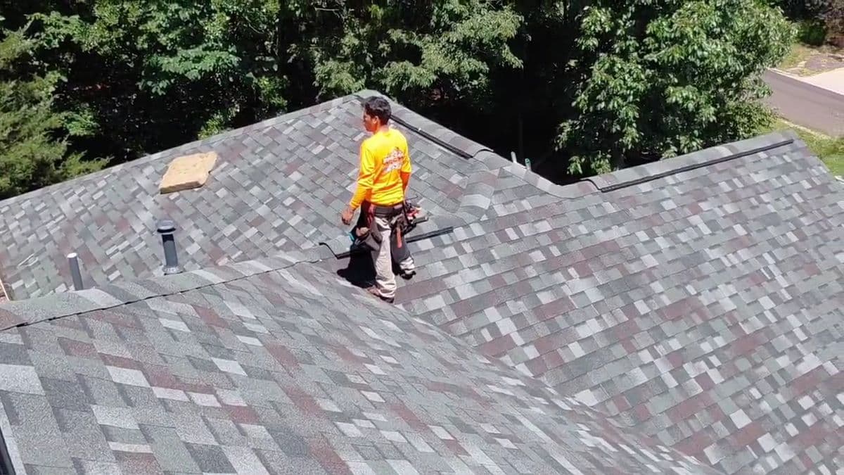 Crew member walking the ridge of a finished multi-tone shingle roof, tool belt on
