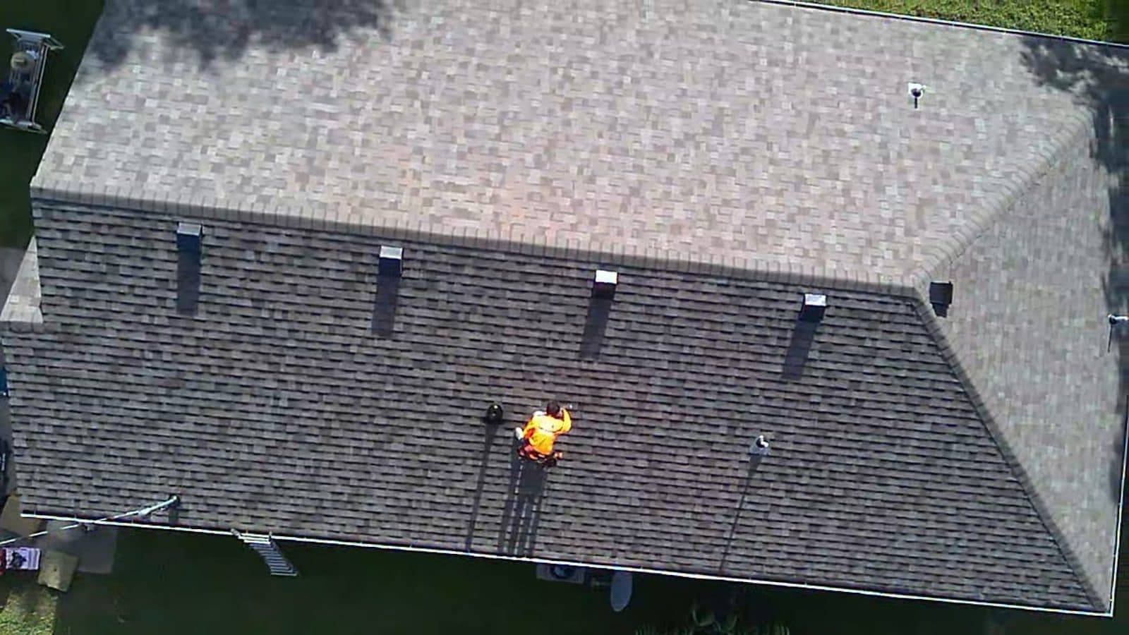 Drone view of a finished shingle roof with a crew member wrapping up on the slope
