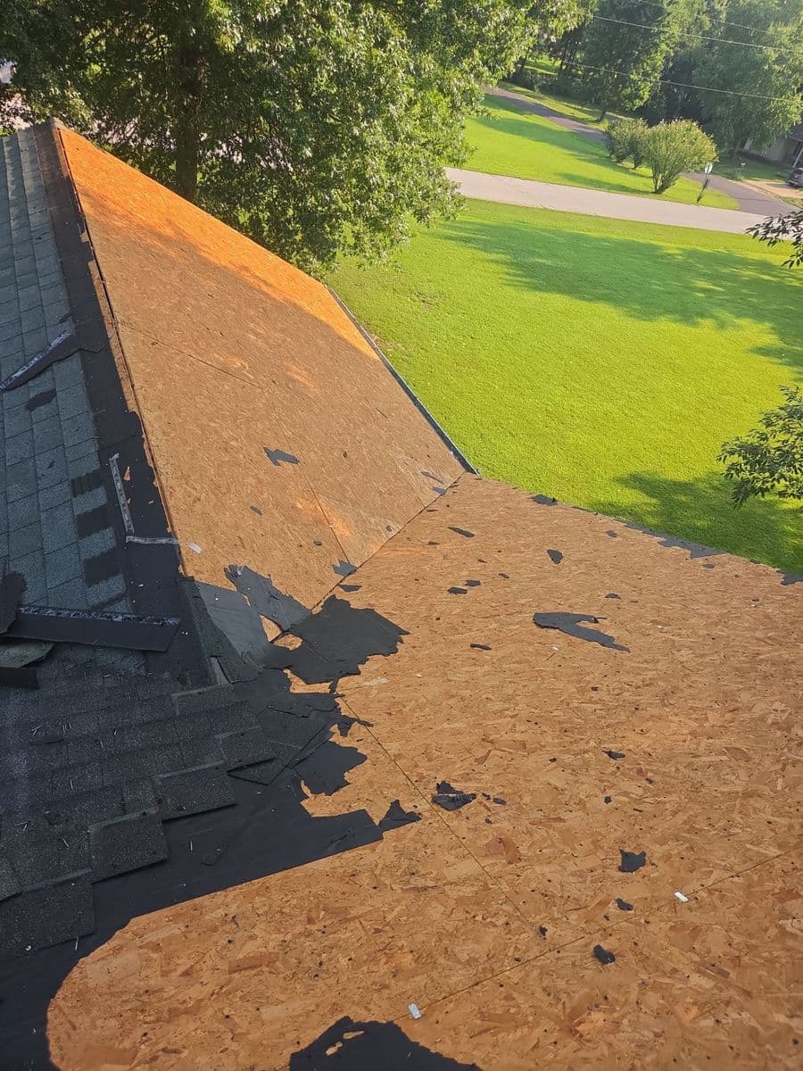 Half-stripped roof with the old shingle courses on one plane and fresh decking exposed on the next