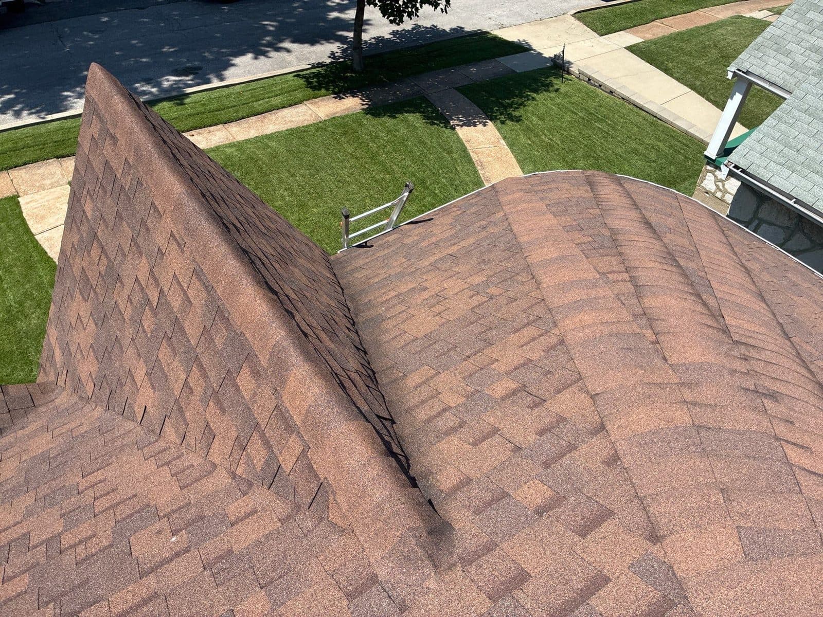 Finished terracotta-blend architectural shingles running up to a clean hip and ridge, a ladder at the eave and the street beyond
