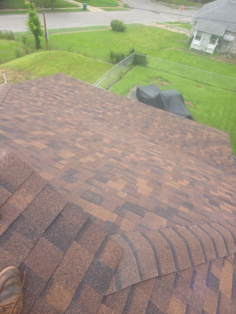 Finished autumn-blend shingle field and capped hip seen from the ridge, back yard and road below