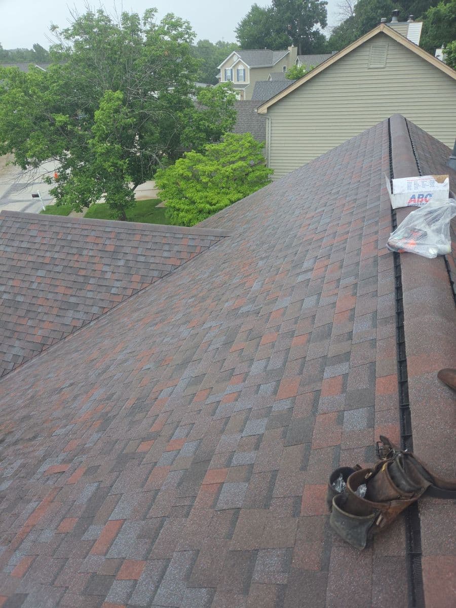 Ridge run on the finished roof with a leather tool belt and a bundle of ridge cap left on the slope